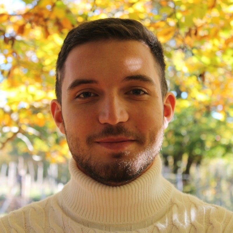 Person wearing a white turtleneck sweater with autumn foliage in the background.